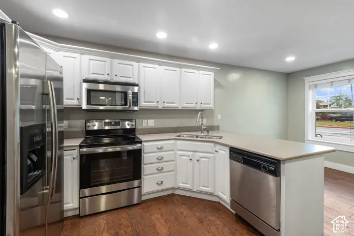 Modern kitchen featuring white cabinetry with brushed nickel hardware, stainless steel appliances including a gas range and dishwasher, granite-style countertops, undermount sink with chrome faucet, recessed ceiling lighting, and wood-finish flooring thro