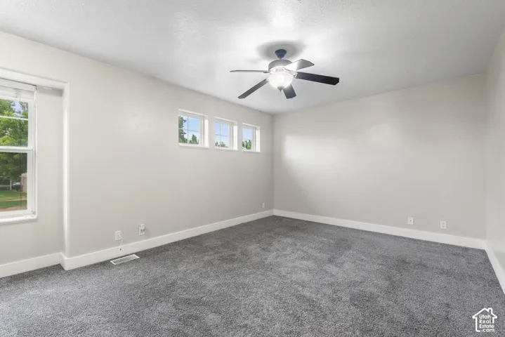 Recessed ceiling fan with integrated lighting, multiple windows providing natural illumination, light-toned wall finishes, and grey carpeting