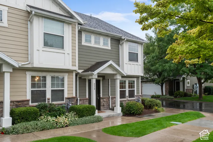 Two-story townhome with bay window, stone veneer accents, covered entry, and landscaped frontage
