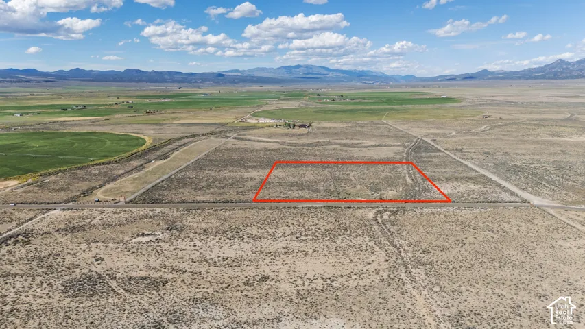 Expansive desert property featuring a defined boundary, mountain range backdrop, and adjacent cultivated fields