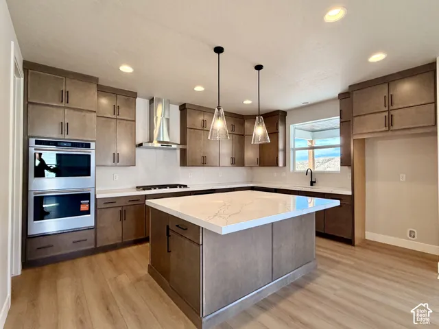 Kitchen featuring wood-finish cabinetry, stainless steel double ovens, a central island with a light-toned countertop, a gas cooktop, and wood-finish flooring