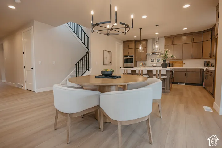 Open-concept kitchen and dining area featuring wood-finish flooring, matte-finish cabinetry, a central island with integrated seating, a multi-arm chandelier, and a staircase with metal railings