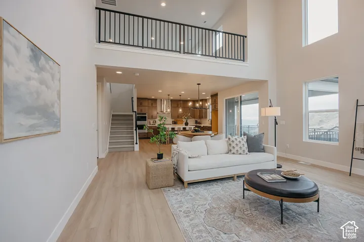 Double-height ceiling, open-concept floor plan, wood-finish flooring, metal staircase railing, and large windows