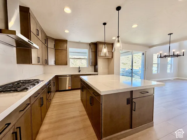 Spacious kitchen featuring an expansive island with a white countertop, wood-finish cabinetry with black hardware, wood-finish flooring, and a stainless steel gas range with a matching range hood