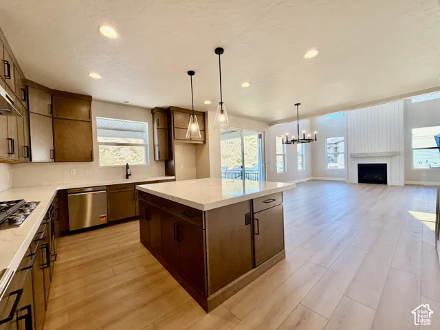 Open-concept kitchen and living area featuring a large center island with a stone countertop, wood-finish flooring, a contemporary fireplace with shiplap detailing, and recessed lighting