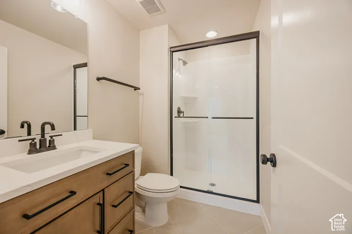 Bathroom featuring a wood-finish vanity with a light stone-style countertop, matte black hardware, a glass-enclosed shower with a subway tile surround, and tile flooring