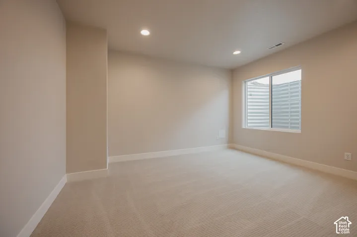 Neutral-toned interior space featuring recessed ceiling lighting, wall-to-wall carpeting, and a wide window with an egress well
