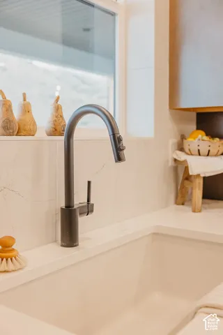 Matte black pull-down kitchen faucet featuring a high-arc design, paired with a white apron-front sink, white composite countertop, and white full-height tile backsplash