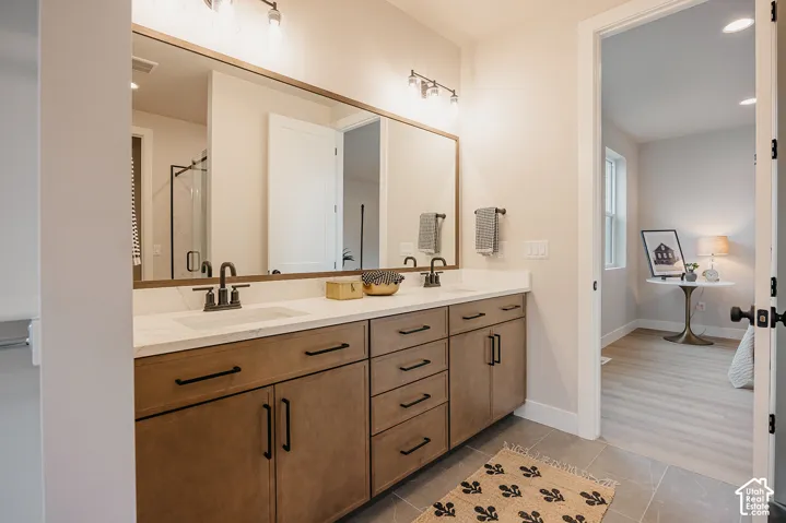 Dual-sink vanity with light-tone wood-finish cabinetry, white stone-composite countertop, matte black hardware, and an oversized rectangular mirror