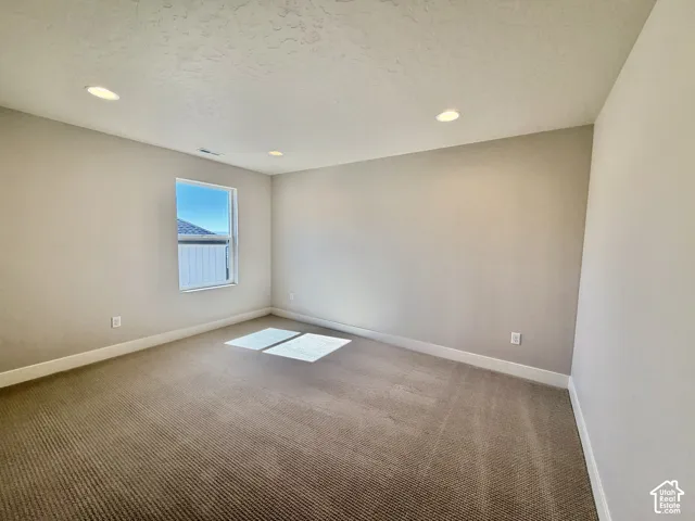 Recessed ceiling lighting, neutral wall tones, window with white trim, and textured carpeting