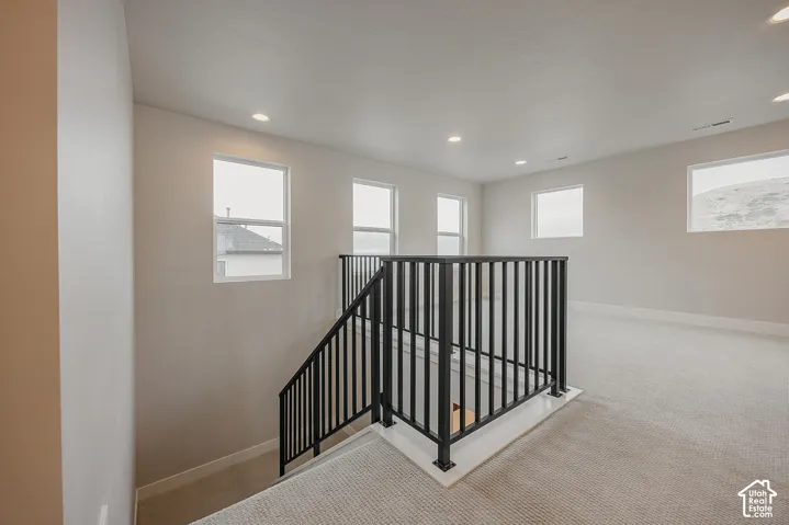 Open loft area featuring wall-to-wall carpeting, recessed ceiling lighting, and matte black metal stair railing
