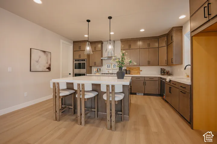 Kitchen featuring flat-panel wood cabinetry, a central island with a solid-surface countertop, built-in double wall ovens, wood-finish flooring, and dual glass pendant lights