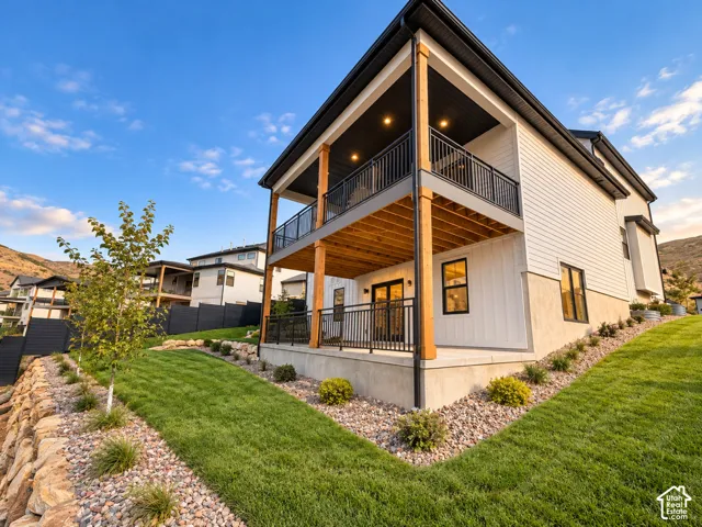Modern exterior featuring white siding, a two-story covered deck with wood accents, and a manicured lawn with natural rock landscaping. Lighting enhanced with ai.