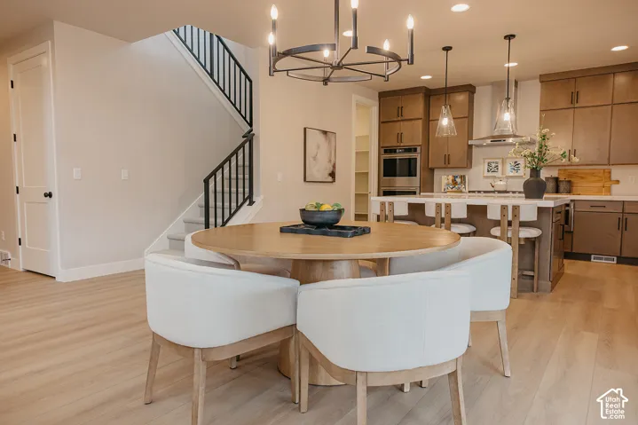 Kitchen featuring wood-finish cabinetry, built-in stainless steel double wall ovens, a center island with pendant lighting, and wood-finish flooring, complemented by a decorative metal chandelier and a staircase with matte black metal balusters