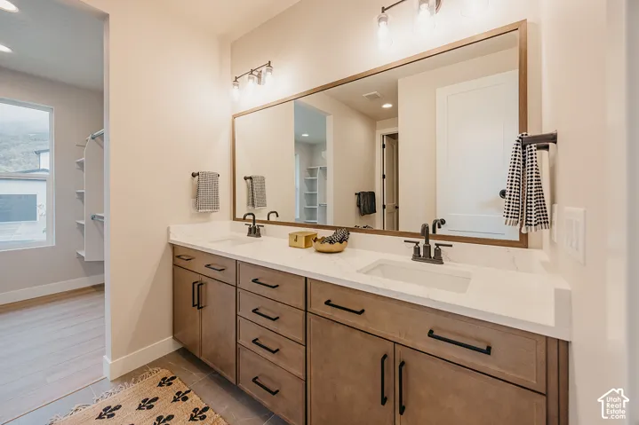 Double vanity featuring light-toned wood cabinetry, stone-finish countertops, undermount sinks, matte black hardware, and an expansive wall-to-wall mirror