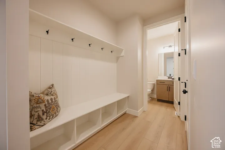 Built-in mudroom bench with integrated cubbies and vertical paneling, topped with wall-mounted hooks and a shelf, featuring wood-finish flooring