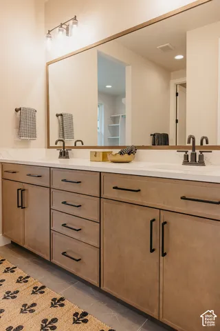Dual-sink vanity featuring light wood cabinetry, white stone countertops, matte black hardware, and a wood-trimmed wall-to-wall mirror