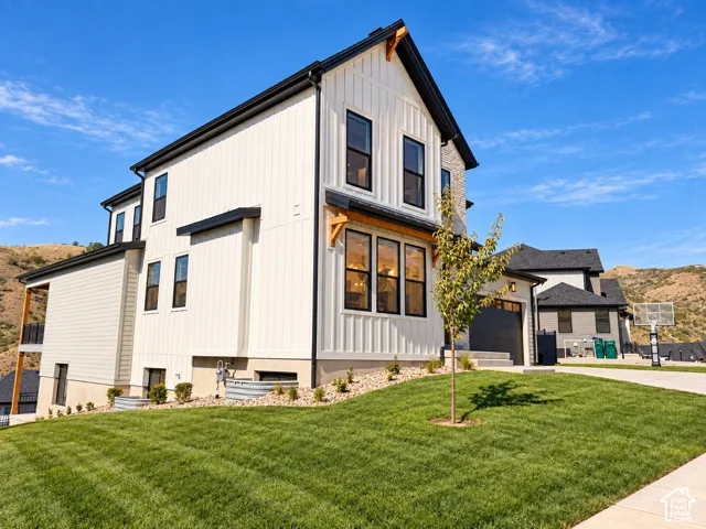 Modern farmhouse exterior featuring vertical board and batten siding, dark trim, a stone chimney, and a multi-level design. Lighting enhanced with ai.