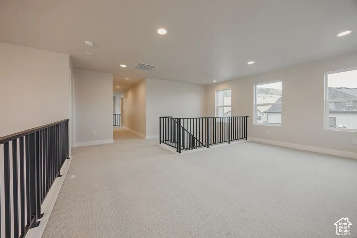 Open-concept area featuring neutral wall-to-wall carpeting, recessed ceiling lighting, and black metal stair railings