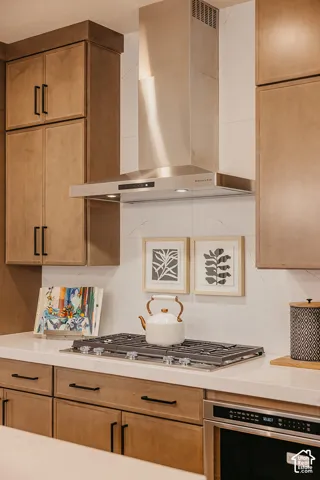 Custom cabinetry with matte black hardware, stone-finish countertops, full-height stone-finish backsplash, stainless steel gas cooktop, and stainless steel chimney-style range hood