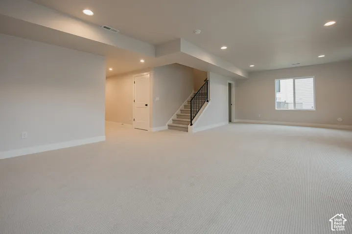 Open-concept interior featuring neutral wall tones, wall-to-wall carpeting, recessed ceiling lighting, a staircase with a metal baluster railing, and a single-pane window