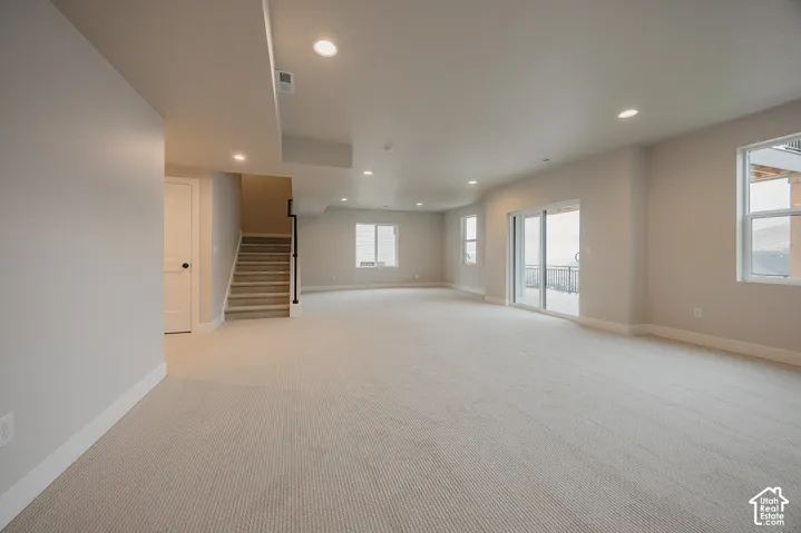 Expansive open-concept space featuring neutral carpeting, recessed ceiling lighting, multiple large windows, and a sliding glass door