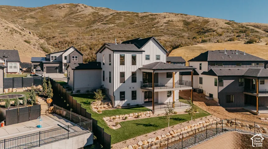 Modern farmhouse exterior featuring vertical white siding, black window trim, two levels of covered outdoor balconies, and tiered landscaping set against a mountainous backdrop