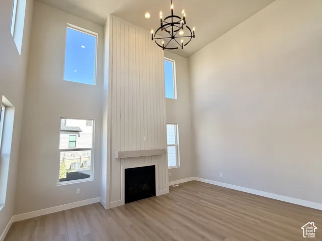 Soaring ceilings, large windows, wood-finish flooring, fireplace with white shiplap surround, and a wrought iron chandelier