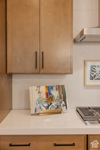 Custom cabinetry with matte black pulls, light-toned stone-surface countertops, matching stone-surface backsplash, and a stainless steel range hood