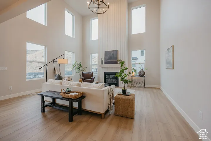 Living area featuring vaulted ceilings, floor-to-ceiling vertical shiplap fireplace surround, expansive windows, wood-finish flooring, and a multi-arm chandelier