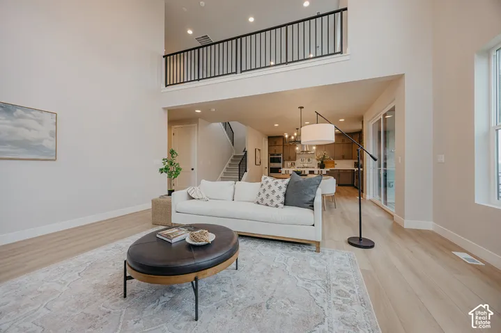 Double-height ceiling, open-concept floor plan, wood-finish flooring, recessed lighting, and metal-rail interior balcony