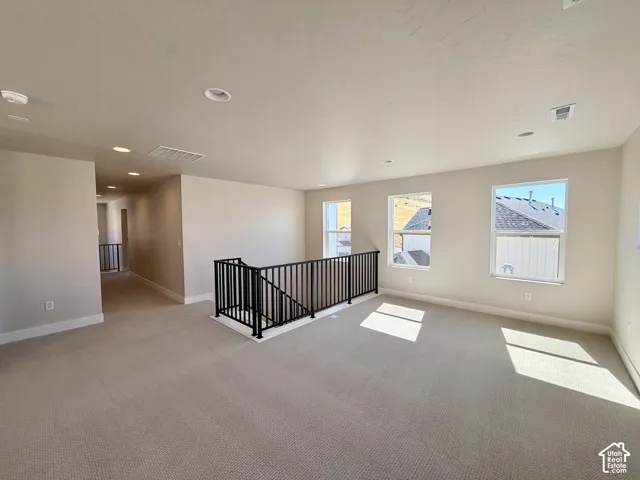Open loft area featuring neutral-toned carpeting, multiple windows, recessed lighting, and a black wrought iron railing system