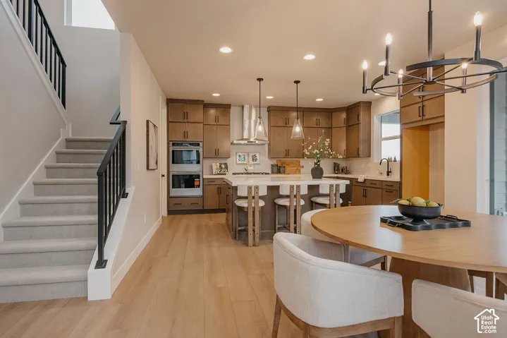 Kitchen featuring wood-finish cabinetry, a center island with stone-surface countertop, built-in double wall ovens, wood-finish flooring, and a decorative metal chandelier