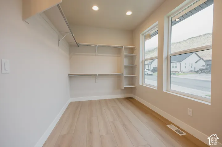 Walk-in storage space featuring wood-finish flooring, recessed lighting, multi-level hanging rods, built-in shelving, and dual windows