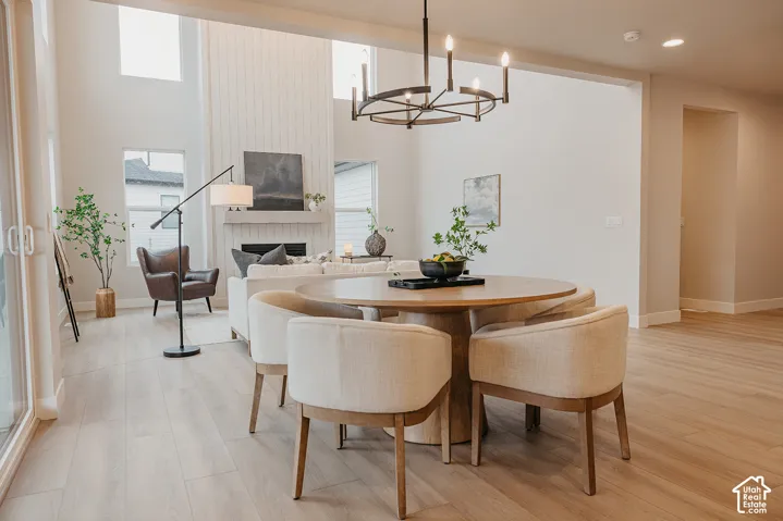 Open-concept living space featuring high ceilings, wood-finish flooring, a vertical shiplap fireplace surround, and a matte black chandelier