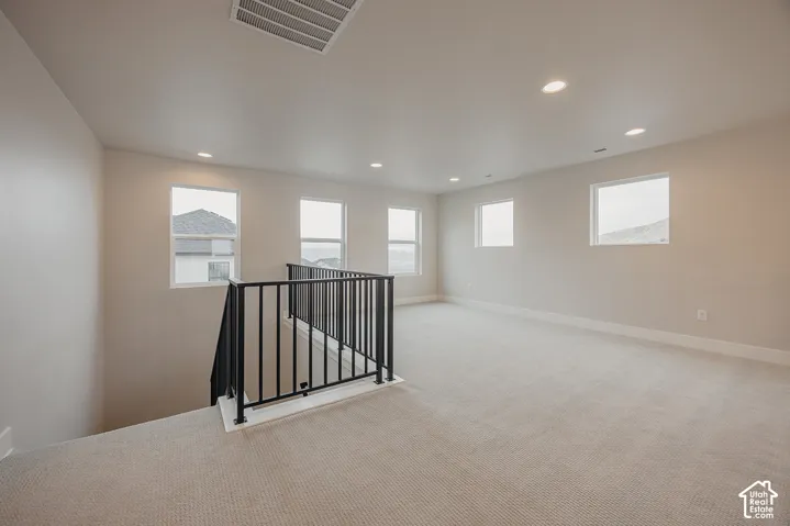Open-concept interior featuring neutral wall tones, recessed lighting, wall-to-wall carpeting, and a matte black metal stair railing