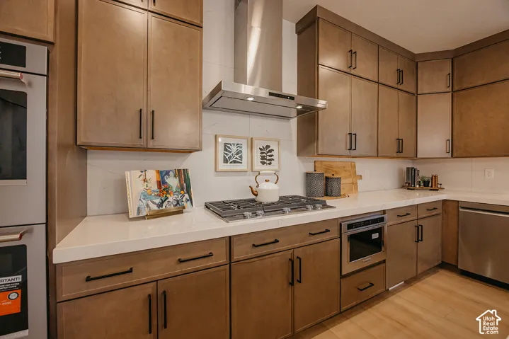 Kitchen featuring custom cabinetry with matte black hardware, stainless steel gas cooktop, professional-grade range hood, built-in wall oven, and light-toned countertops