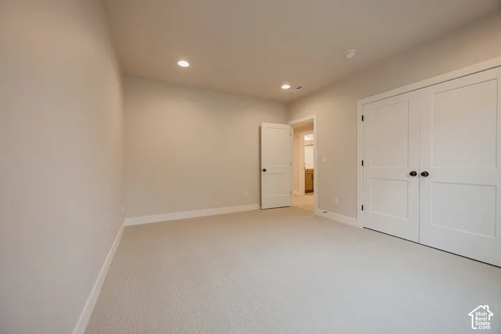 Neutral-toned interior room featuring wall-to-wall carpeting, recessed ceiling lighting, two-panel interior doors, and double-door closet entry