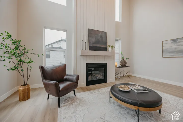 High-ceiling living area featuring a floor-to-ceiling vertical plank fireplace surround, a wood-finish mantel, an integrated fireplace, and wood-finish flooring