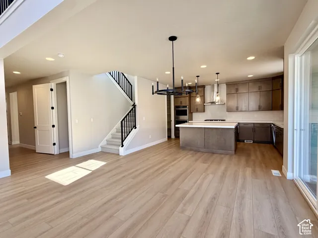 Open-concept living area with wood-finish flooring, a modern kitchen with a central island, stainless steel appliances, and built-in cabinetry