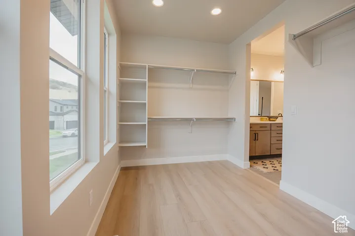 Walk-in closet featuring white custom built-in shelving, dual-tier hanging rods, wood-finish flooring, recessed lighting, and large windows