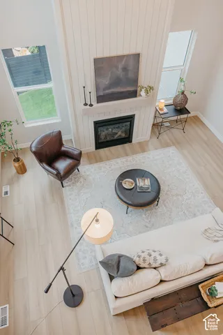 Double-height ceiling, vertical shiplap fireplace surround, wood-finish flooring, and expansive windows