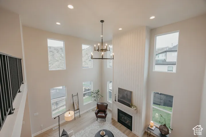 Two-story height ceiling with multi-level windows, floor-to-ceiling vertical plank fireplace surround, iron chandelier, wood-finish flooring, and black metal balcony railing