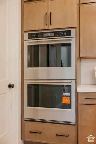 Built-in stainless steel double wall oven featuring a digital control panel, integrated within custom wood cabinetry with matte black hardware and a solid surface countertop