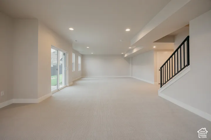 Open floor plan featuring neutral wall-to-wall carpeting, recessed ceiling lighting, sliding glass door, and black metal staircase railing