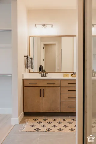 Wood-finish vanity cabinet with matte black hardware, white countertop, integrated basin, and large rectangular mirror with wood-tone frame, illuminated by a three-light fixture
