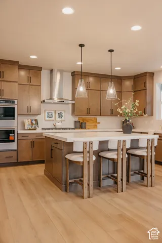 Kitchen featuring stained wood cabinetry, quartz countertops, a central island, recessed ceiling lighting, and stainless steel wall-mounted oven and range hood