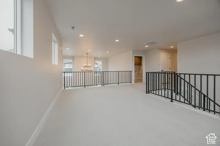 Open-concept space featuring recessed lighting, wall-to-wall carpeting, black metal balustrade railing, and neutral-toned wall paint