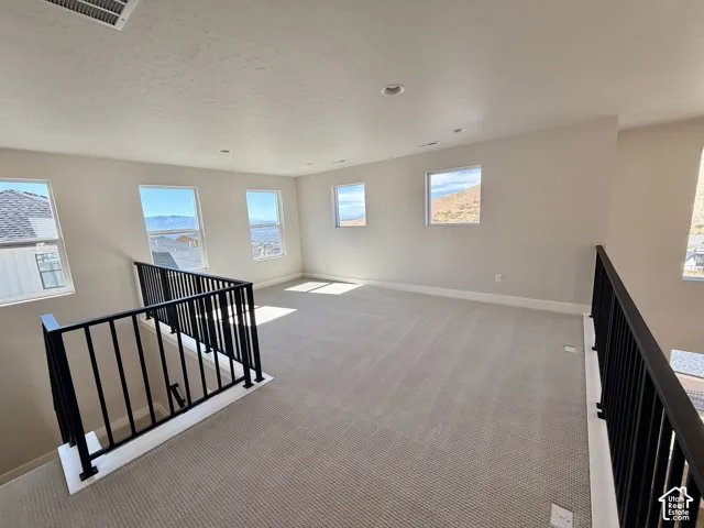 Open loft area featuring neutral carpeting, recessed lighting, multiple windows, and a black metal railing