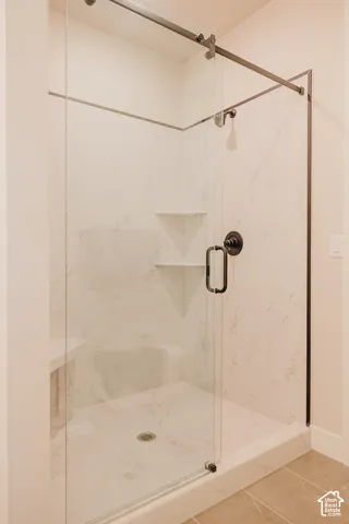 Walk-in shower featuring large-format wall paneling, a sliding frameless glass door, integrated corner shelving, a built-in seat, and bronze-tone fixtures